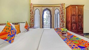 Una habitación de hotel con una cama, almohadones coloridos, una alfombra estampada y un armario de madera.