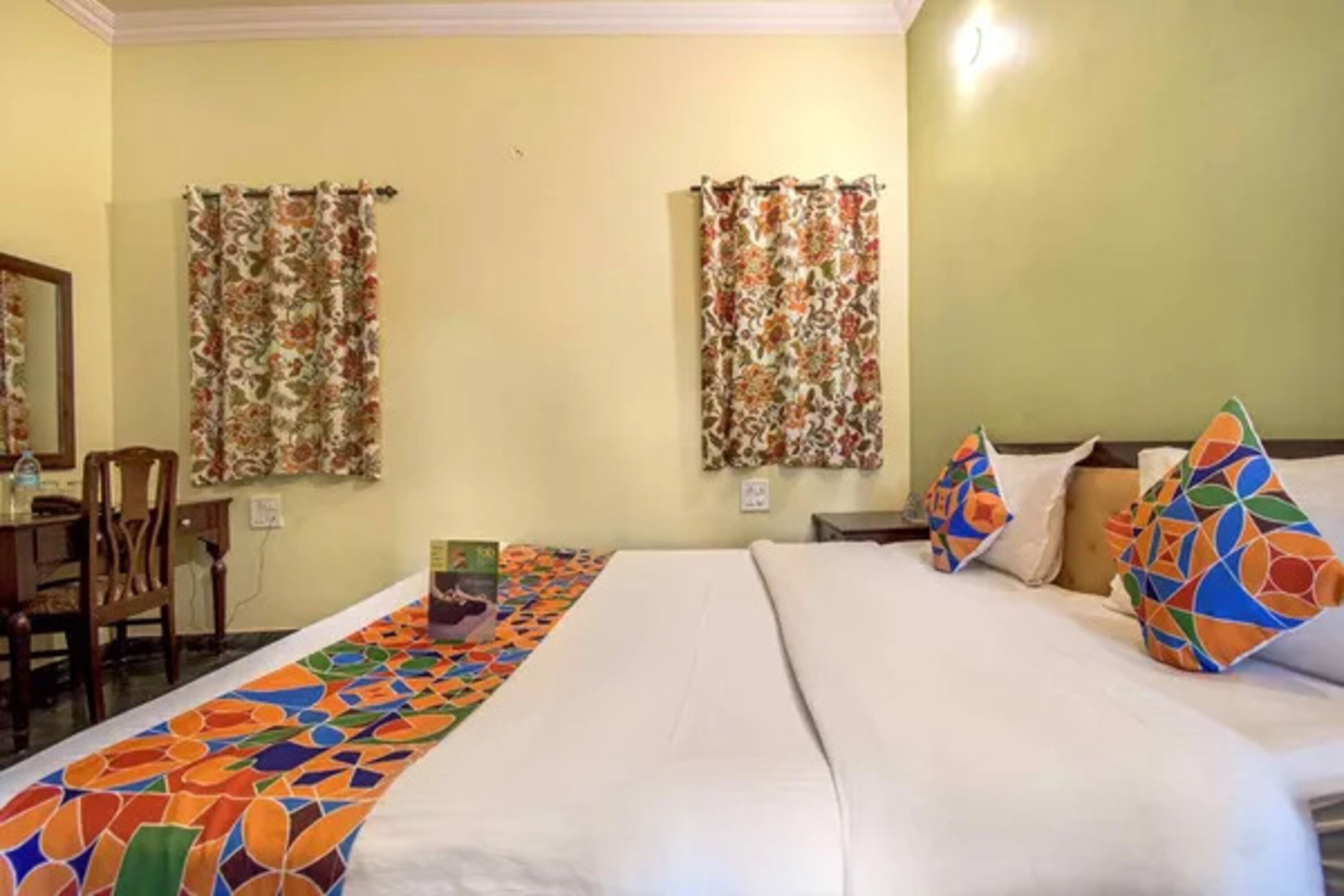 Una habitación de hotel con una cama grande, dos cortinas, una mesita pequeña y una alfombra colorida.