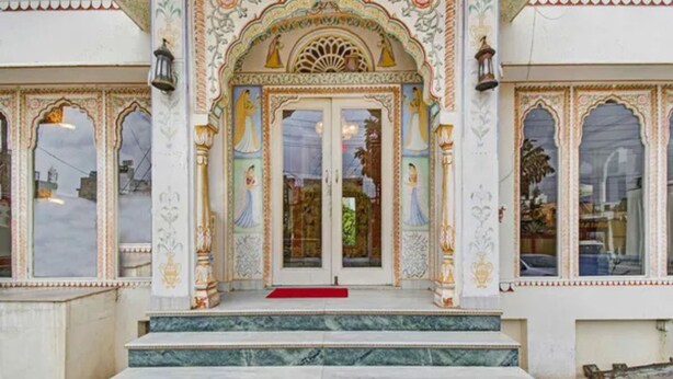 Un edificio con detalles arquitectónicos ornamentales, incluyendo una entrada decorativa con alfombra roja y escalones de mármol.