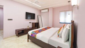 A bedroom with a bed, a TV, a ceiling fan, a window with blinds, and a bedside table. - FabHotel The White Cliff Inn - Near Max Hospital Saket (New Delhi)