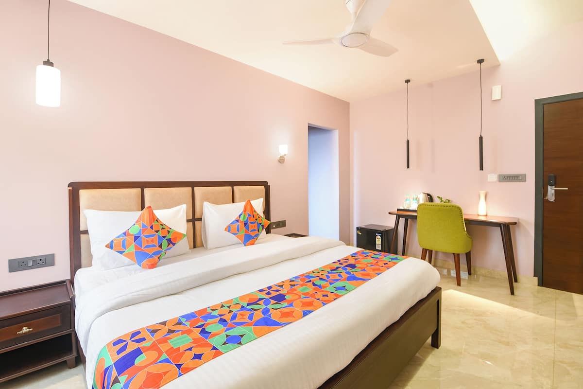 A hotel room with a bed, a desk, a chair, a ceiling fan, and a door.