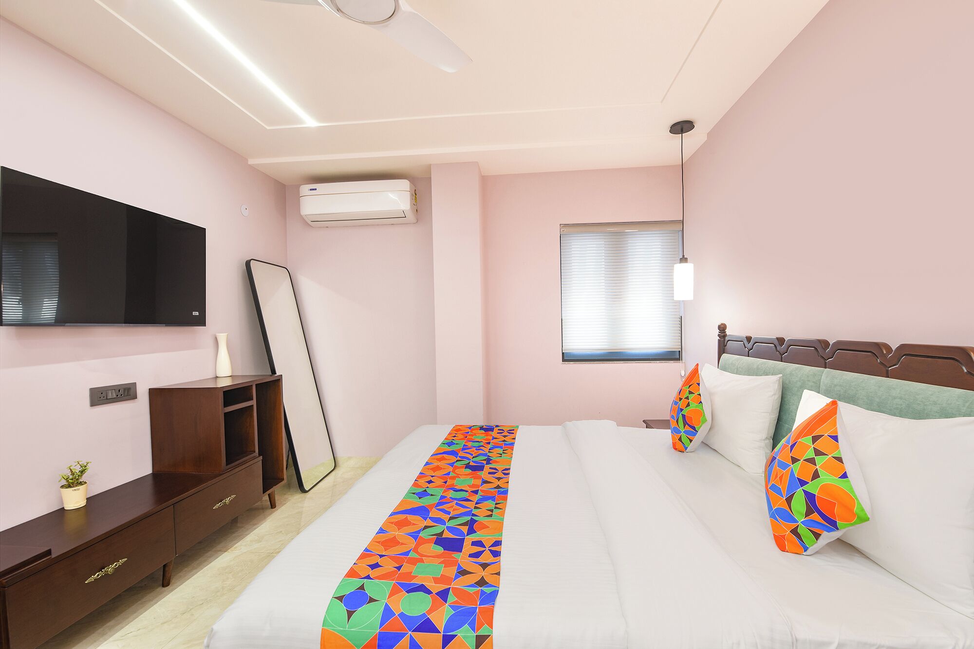 Une chambre à coucher avec un lit, une télévision, un miroir, une commode et une fenêtre.