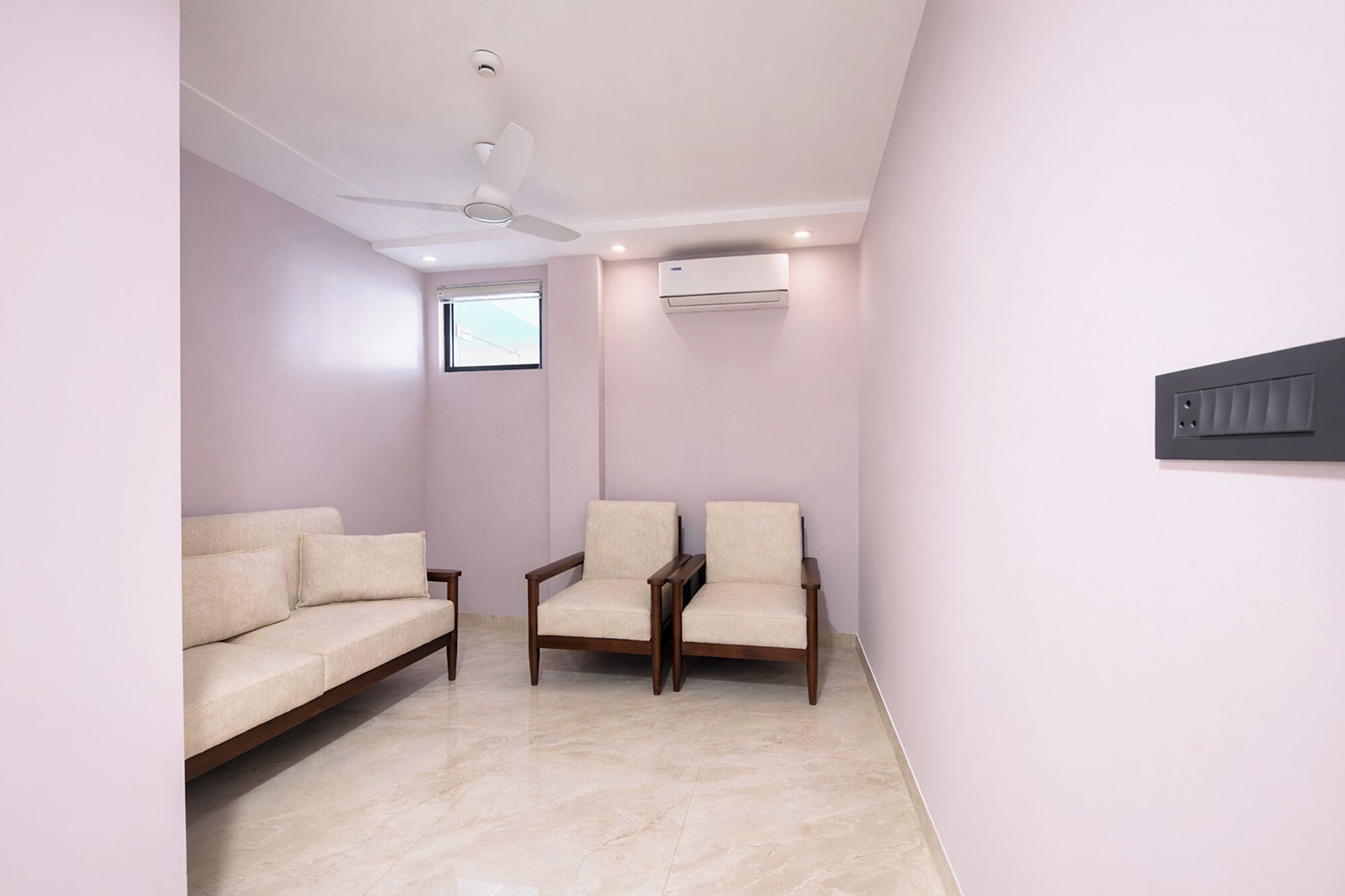 A room with a sofa, two chairs, a ceiling fan, an air conditioning unit, and a window.
