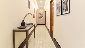 A hallway with a marble floor, a console table with a vase and books, framed artwork on the walls, and a wooden door at the end. - FabHotel D3 - Vaishali Nagar (Jaipur)
