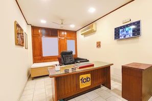 Un mostrador de recepción de hotel con un letrero de 'fab hotels', un ventilador de techo, un equipo de aire acondicionado, un televisor montado en la pared y una ventana con persianas.
