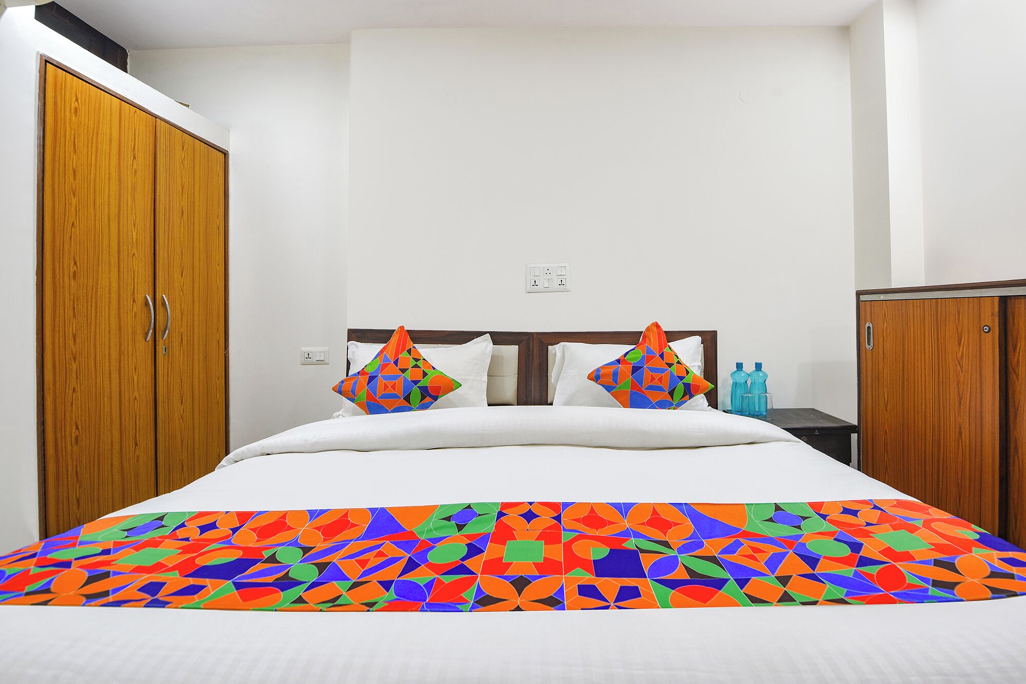 A bedroom with a bed, two wooden wardrobes, and a nightstand with water bottles.