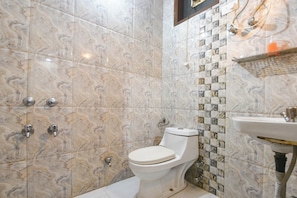 Une salle de bain carrelée de marbre, avec des toilettes, un lavabo et un espace douche.