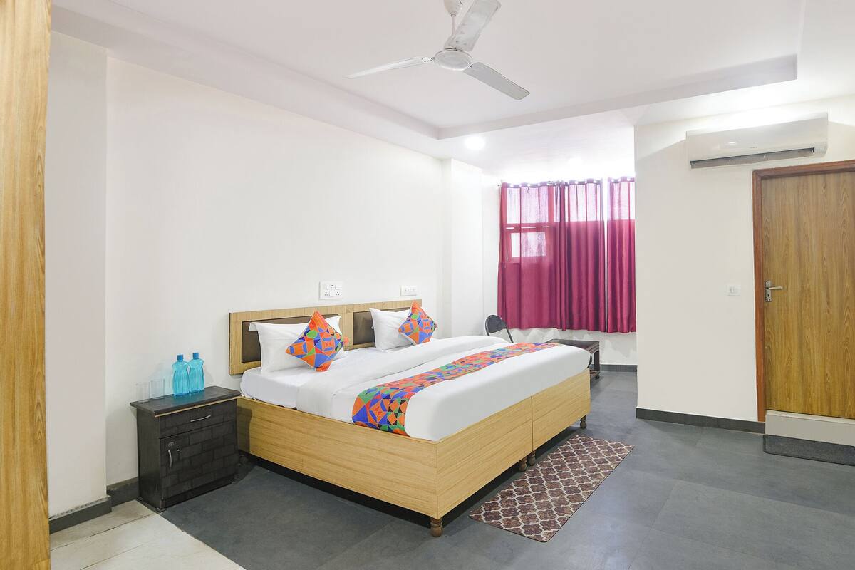 A bedroom with a bed, a nightstand, a ceiling fan, a window with curtains, and an air conditioning unit.