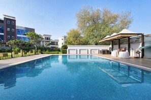 Ein Swimmingpool mit glatter, blauer Wasseroberfläche, umgeben von modernen Gebäuden und Grünpflanzen.