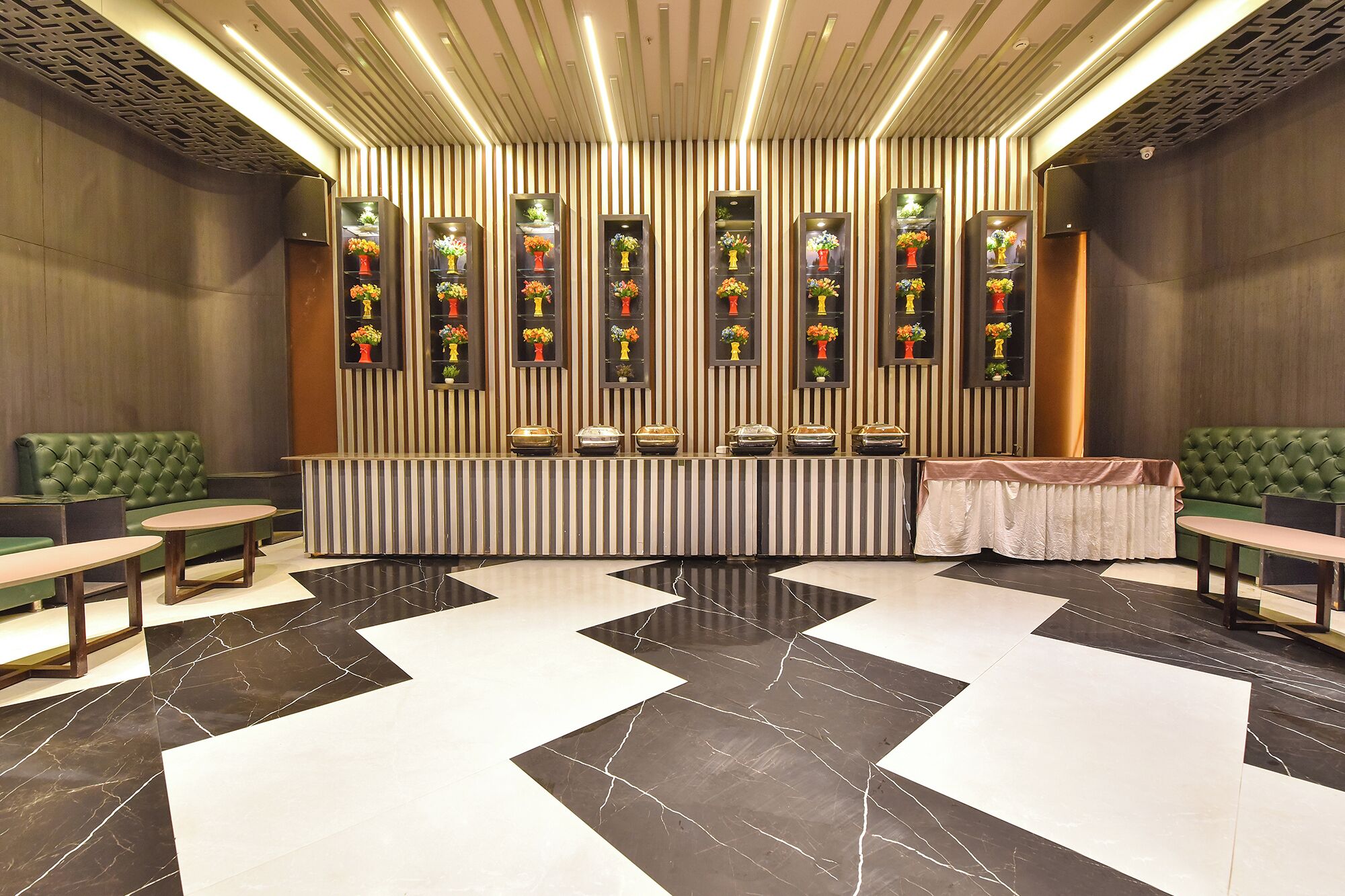 Un vestíbulo de hotel con paredes a rayas, un mostrador de recepción central, asientos verdes y un suelo de baldosas blanco y negro.