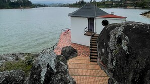 A small building with a red roof and a brick pathway leading to it, situated by a calm body of water. - Finca La Cruz (El Penol)