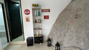 A room with a tiled floor, a black door, a shelf with various items, and a large rock wall. - Finca La Cruz (El Penol)
