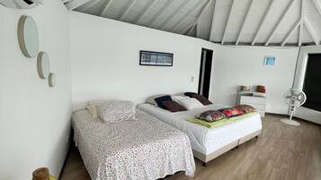 Un dormitorio con techo inclinado, cama con colcha estampada, mesita de noche con lámpara y aire acondicionado de pared.
