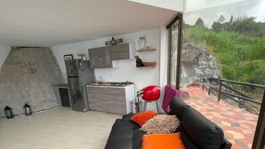 A modern living area with a black sofa, a small round table, and a kitchen in the background. - Finca La Cruz (El Penol)