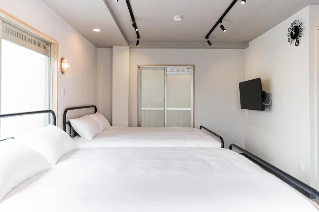 A hotel room with two beds, a sliding door, a mounted TV, and a clock on the wall.