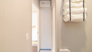 A hallway with a wall-mounted air conditioner, a towel rack with folded towels, and a thermostat on the wall.