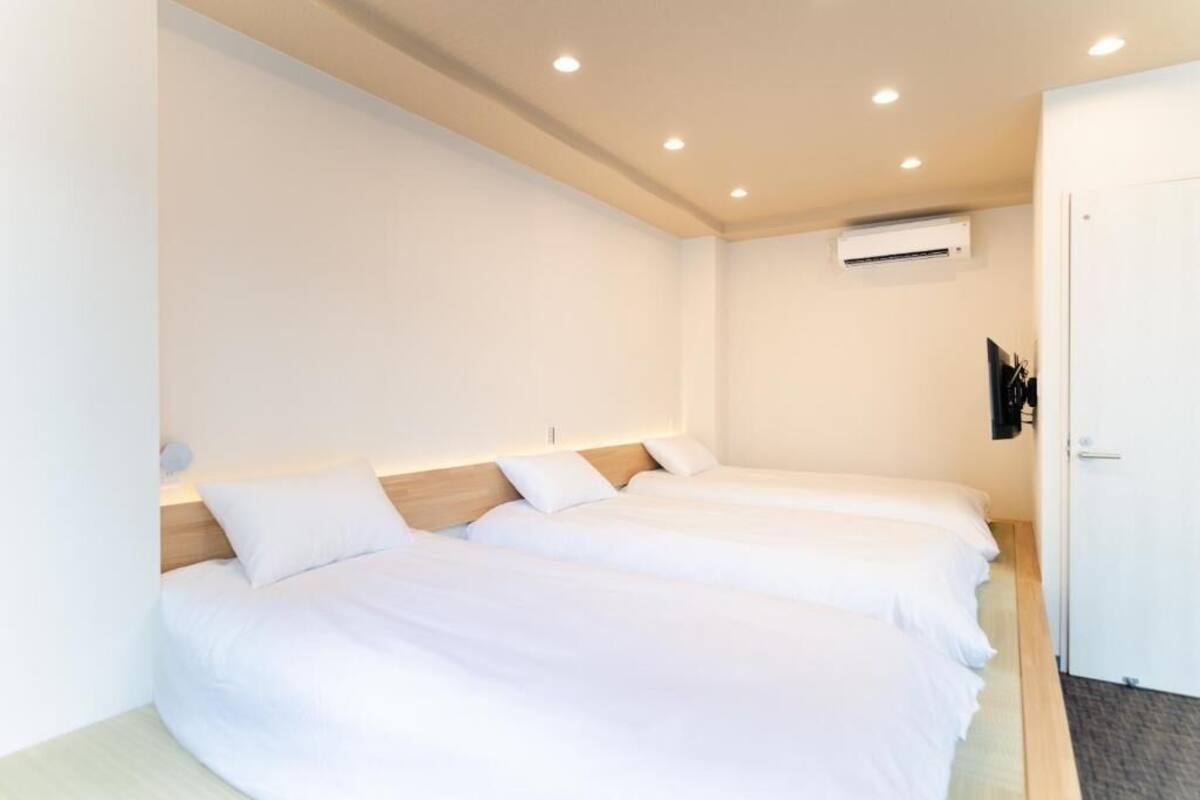 A hotel room with two single beds, a white wall, an air conditioning unit, and a door.