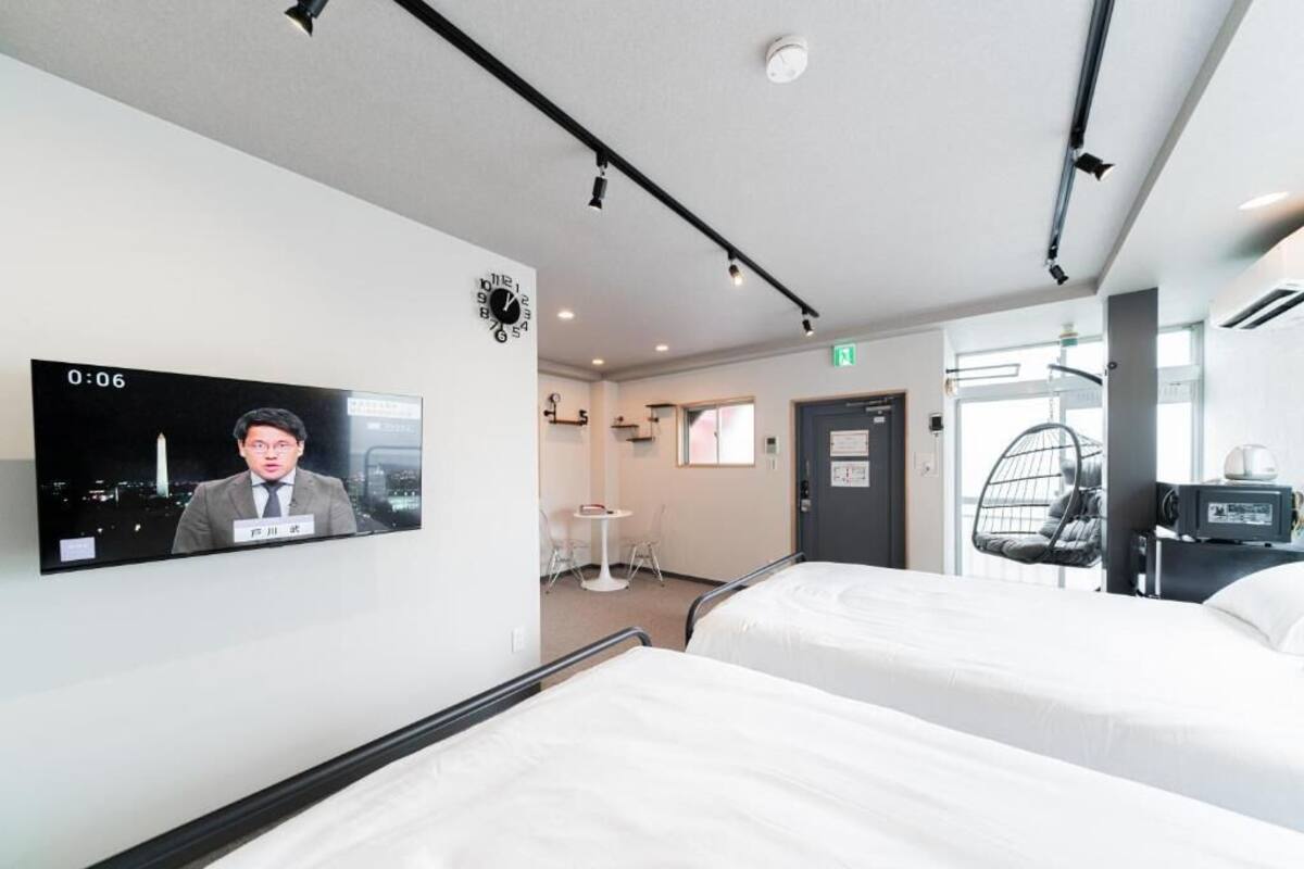 A hotel room with two beds, a television mounted on the wall, a small table with chairs, and a hanging chair.