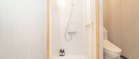 A small, narrow bathroom with a shower, toilet, and two bottles of soap.