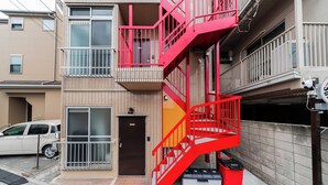 A multi-story building with a red fire escape, a brown door, and a parked car.