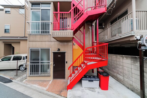 A multi-story building with a red fire escape, a brown door, and a parked car.