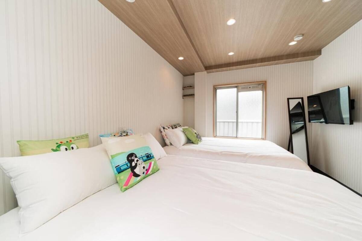 A bedroom with a large bed, two pillows, a television on the wall, and a window.