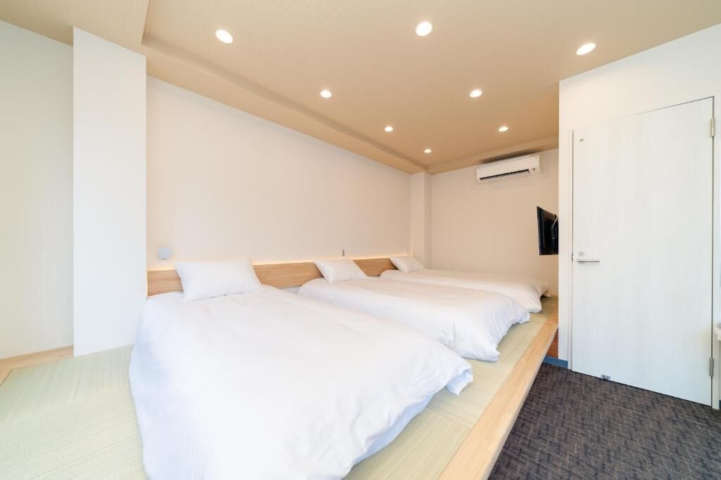 Une chambre d’hôtel avec deux lits, un téléviseur à écran plat fixé au mur et une porte sur le côté droit.