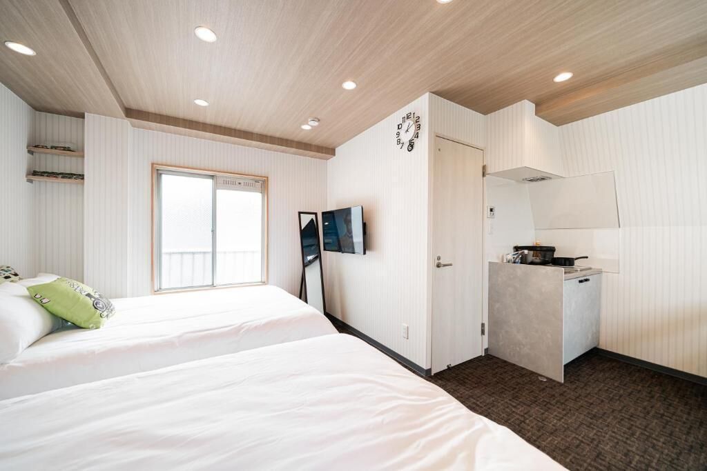 A hotel room with a large bed, a small kitchenette, a TV, and a window.