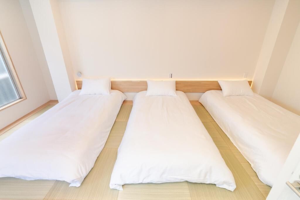 Habitación con tres camas individuales dispuestas contra una pared, cada una con cabecero de madera y ropa de cama blanca.
