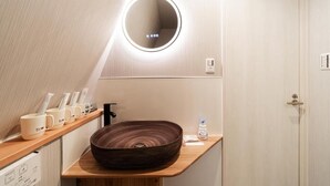 A modern bathroom with a wooden vanity, a round mirror with integrated lighting, and a large, dark wooden bowl sink.