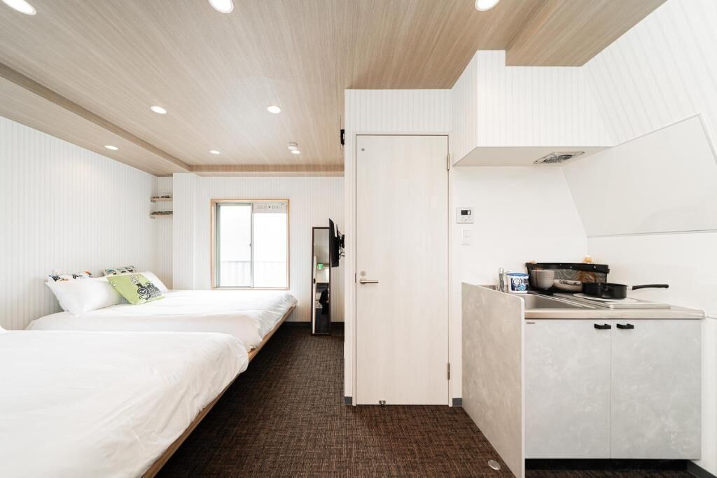 Ein kleines Hotelzimmer mit Bett, einer Küchenzeile und einem durchgegangenen Tür einsehbaren Badezimmer.