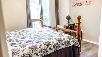 Une chambre à coucher avec un lit en bois, une literie à motifs floraux, une fenêtre avec des rideaux et un tableau accroché au mur.