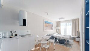 Una habitación de hotel moderna con kitchenette, zona de comedor, cama y un gran ventanal con cortinas.