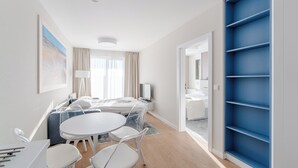 Una habitación de hotel moderna con una cama, una mesa de comedor con sillas, un televisor y un estante azul.