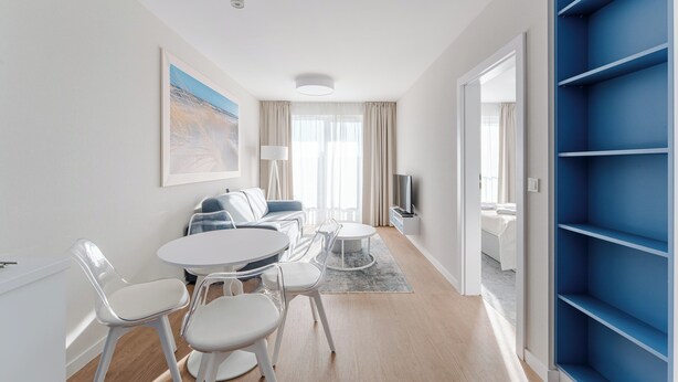 Una sala de estar moderna con una mesa de comedor redonda, sillas blancas, un sofá y un televisor.