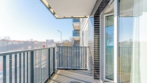 Un balcón con puerta de cristal, baranda metálica y vista al cielo y edificios.