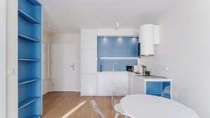 Una cocina moderna con muebles azules y blancos, una mesa de comedor blanca con sillas, y piso de madera.