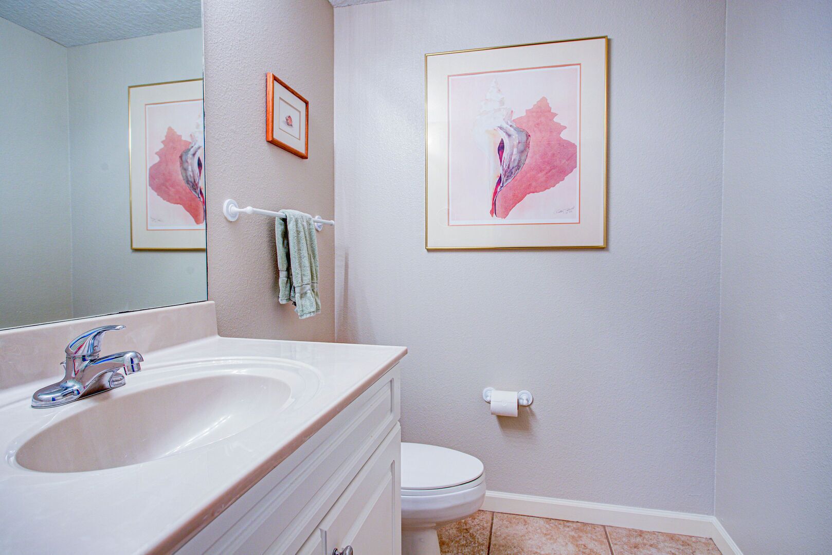 A bathroom with a sink, mirror, toilet, and framed artwork on the wall.