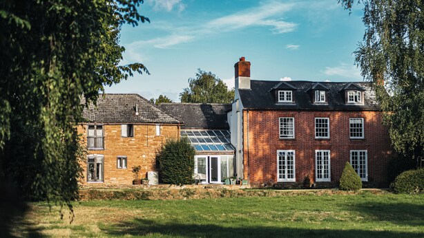 Une maison à deux étages avec une façade en briques, une véranda et une pelouse bien entretenue.