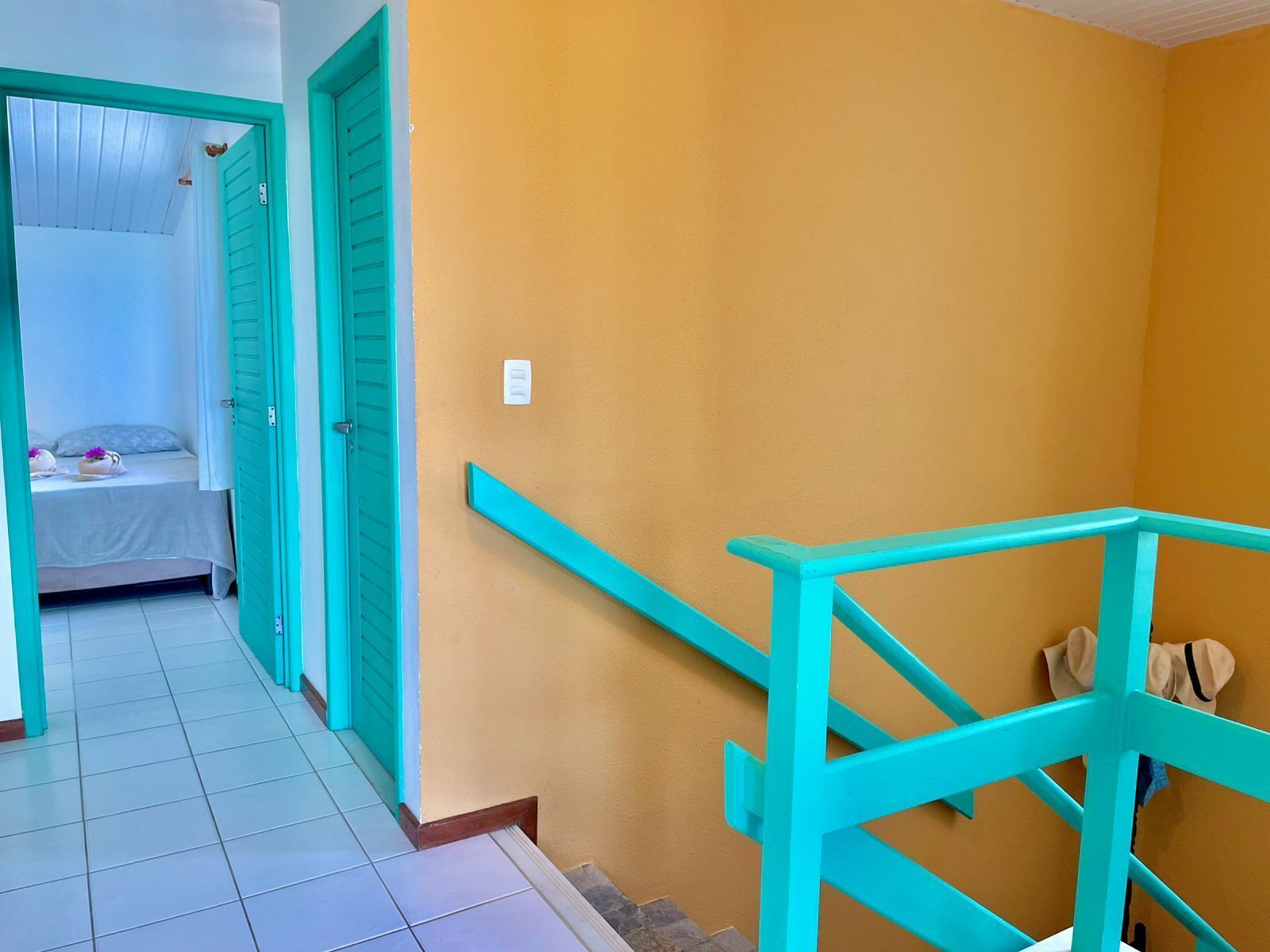 A hallway with a bed, a bathroom, and a staircase with turquoise railings.