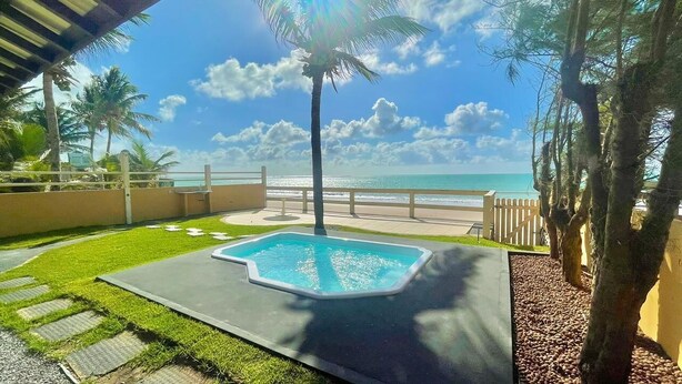 Piscina con vista al océano, rodeada de palmeras y una valla de madera.
