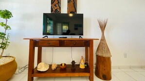 Un mueble bajo de madera para televisor con un televisor de pantalla plana, dos esculturas fijadas a la pared, un estante pequeño con objetos decorativos y un jarrón alto.