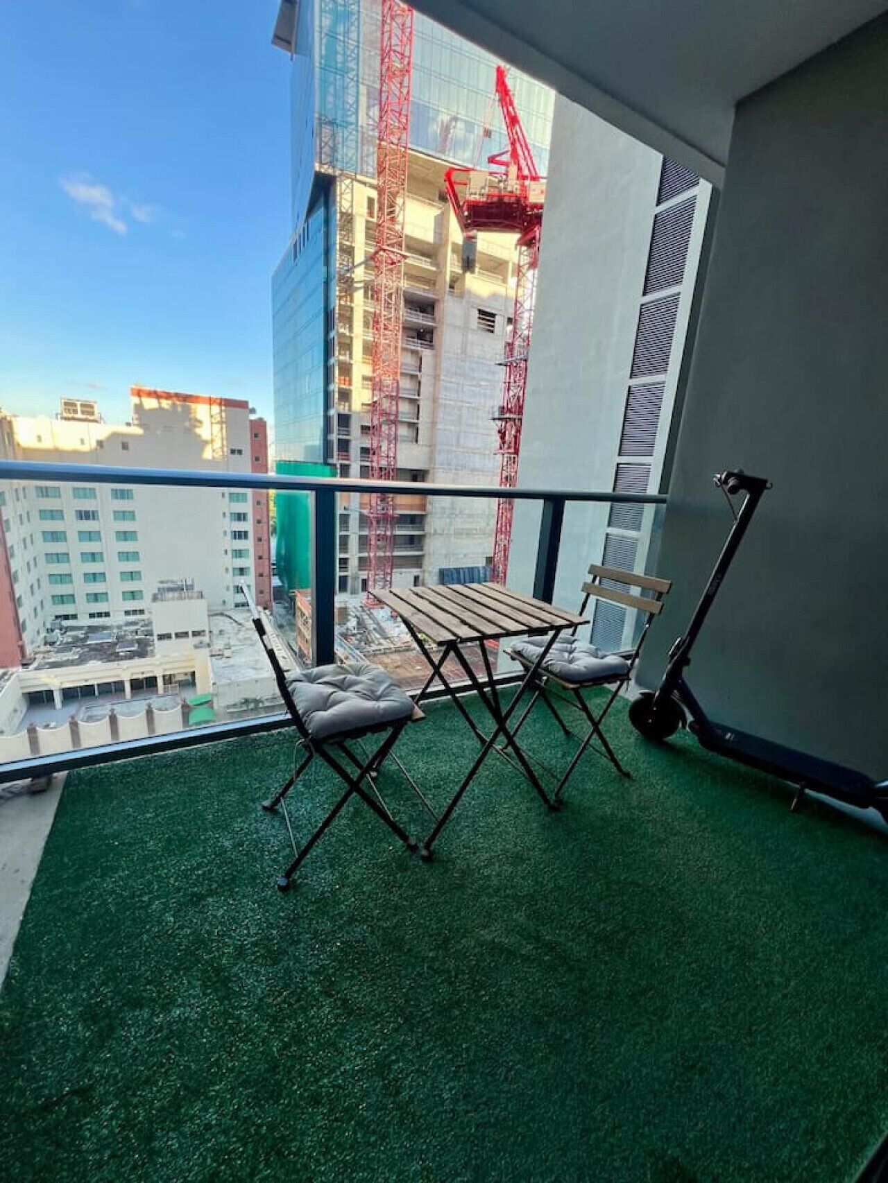 Ein Balkon mit Blick auf eine Baustelle, ein Tisch, zwei Stühle und ein Roller.