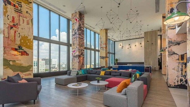 Uma sala ampla com janelas grandes, um conjunto de sofás modernos e iluminação pendente geométrica.