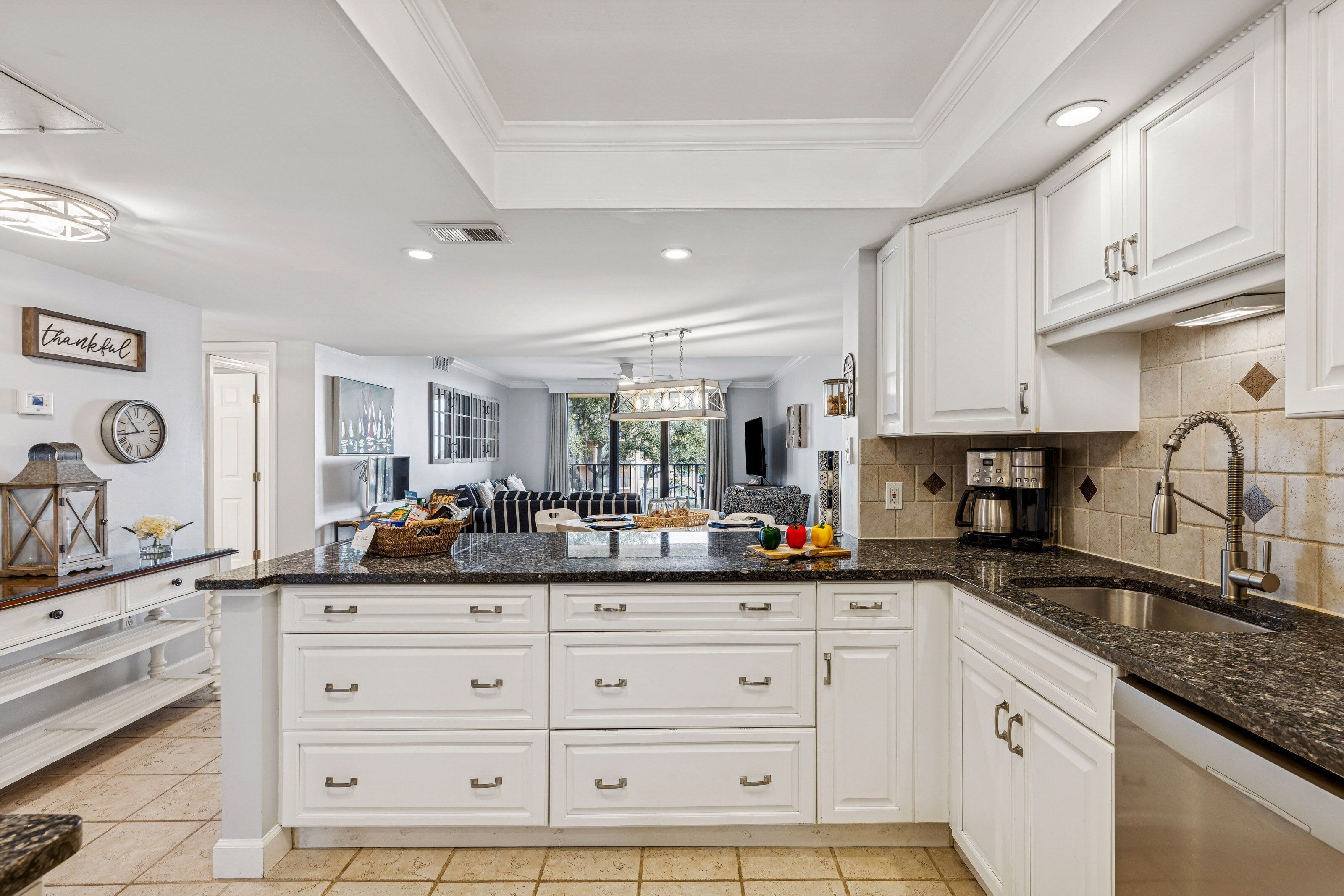 Une cuisine spacieuse dotée de meubles blancs, de plans de travail en granit et d’un grand îlot central muni de nombreux tiroirs.