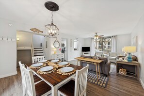 A dining area with a wooden table set for six, white chairs, and a chandelier. - 2BR Seascape Villa, 0.2 Mi to Private Beach Amenities, Walk to Dining & Shops (Hilton Head Island)