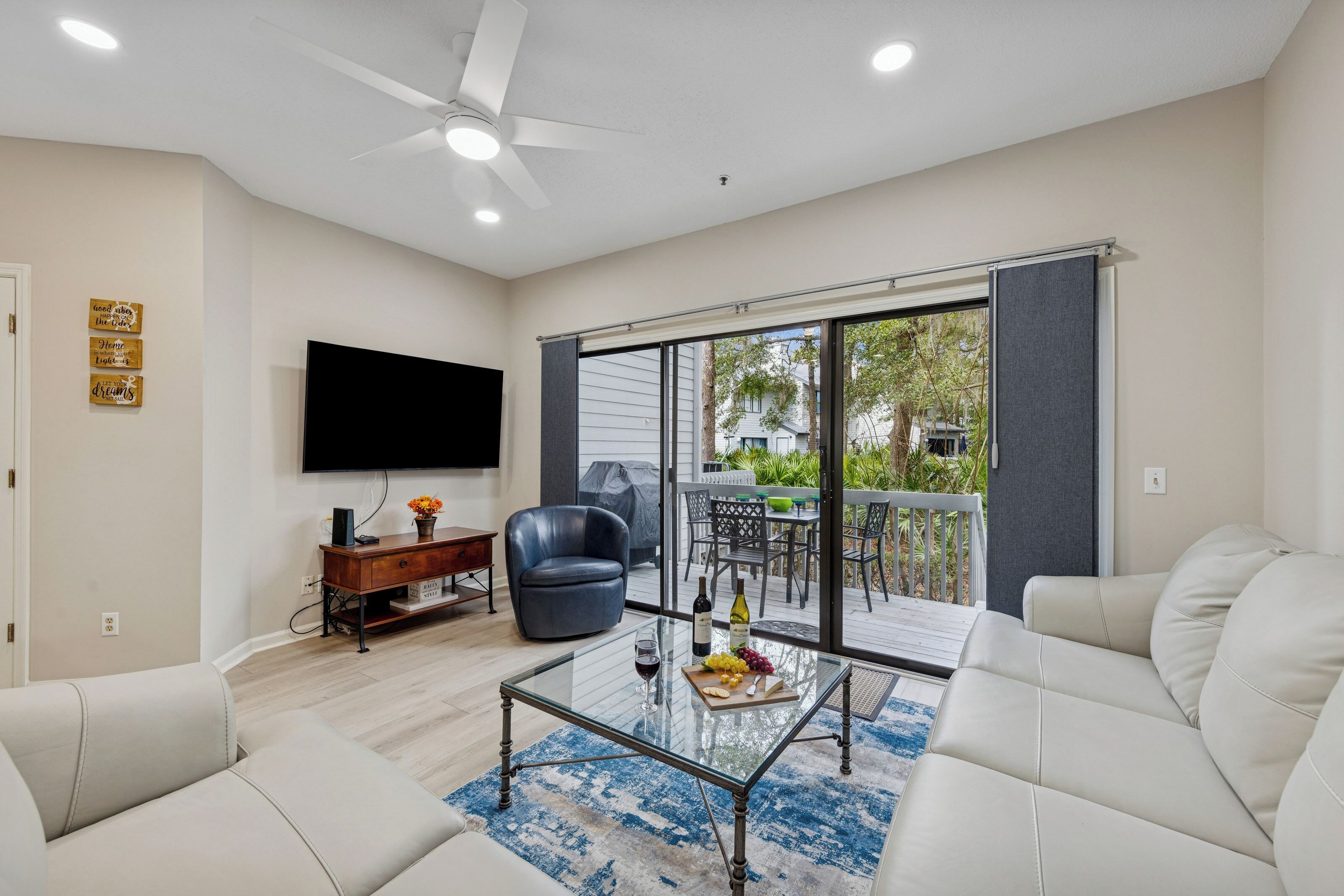 A modern living room with a flat-screen TV, leather sofa, glass coffee table, and a balcony with sliding glass doors.