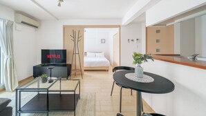 A modern hotel room with a bed, a TV displaying 'NETFLIX', a small table with a plant, and a kitchenette area. - E-US NAEBO STATION 103 (Sapporo)