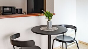 A modern kitchen with a microwave, a black refrigerator, and a small dining area with two black chairs and a round table. - E-US NAEBO STATION 103 (Sapporo)