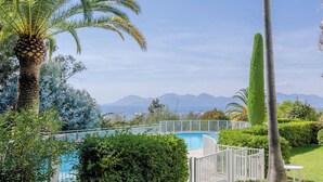 Ein Pool, umgeben von üppiger Vegetation und Palmen, mit freiem Blick auf entfernte Berge.